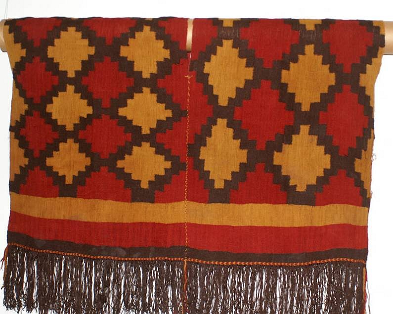 Peru, Nazca Tunic with bold stepped/diamond motif in red, brown and gold.
This scaffold-woven poncho is decorated with a series of complete stepped diamonds alternating in red and gold, outlined in brown. The bottom is bordered by gold, red and brown horizontal bands, with a narrow braid of twisted gold on top of a brown fringe. This tunic was made by two different weavers in the same workshop as seen by the slightly different sizes of diamonds.  It's very rare to find a complete tunic intact and unopened.
Media: Textile
Dimensions: Height 34" x Length 42"
$30,000
93076