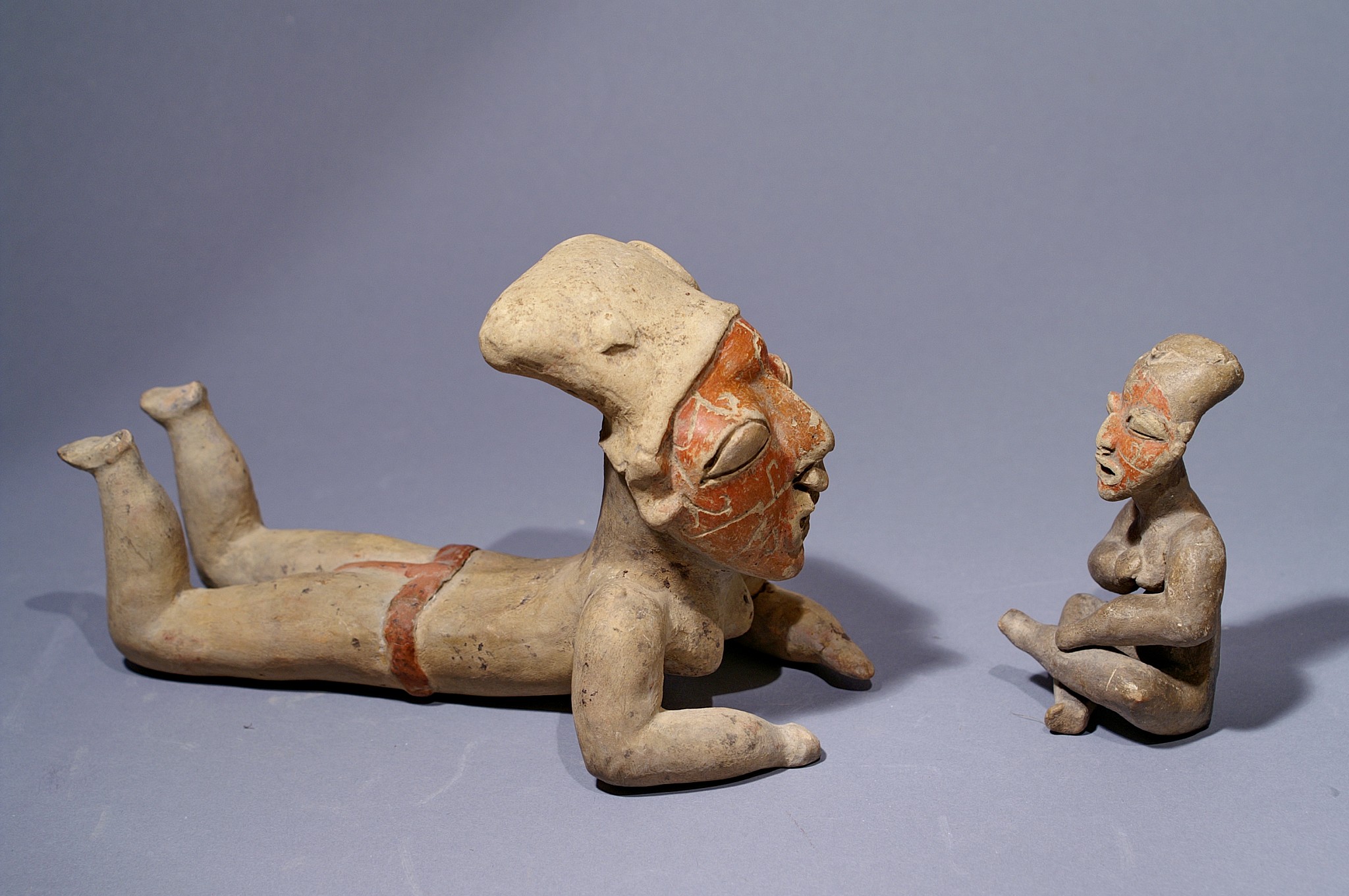 Ecuador, Guangala Pair of Female Figures, one lying down and one seated with hand to breast
The prone position of the larger female may have been borrowed from the neighboring Jamacoaque, but the facial incisions are typical of Guangala figures. The smaller seated female is similarly marked with carved  facial designs. Guangala ceramics are unique in the northern coast for incising such markings on pottery figurines.
Media: Ceramic
Dimensions: Height: 7 3/4" lying down, 3 3/4" seated
$12,000
M7089