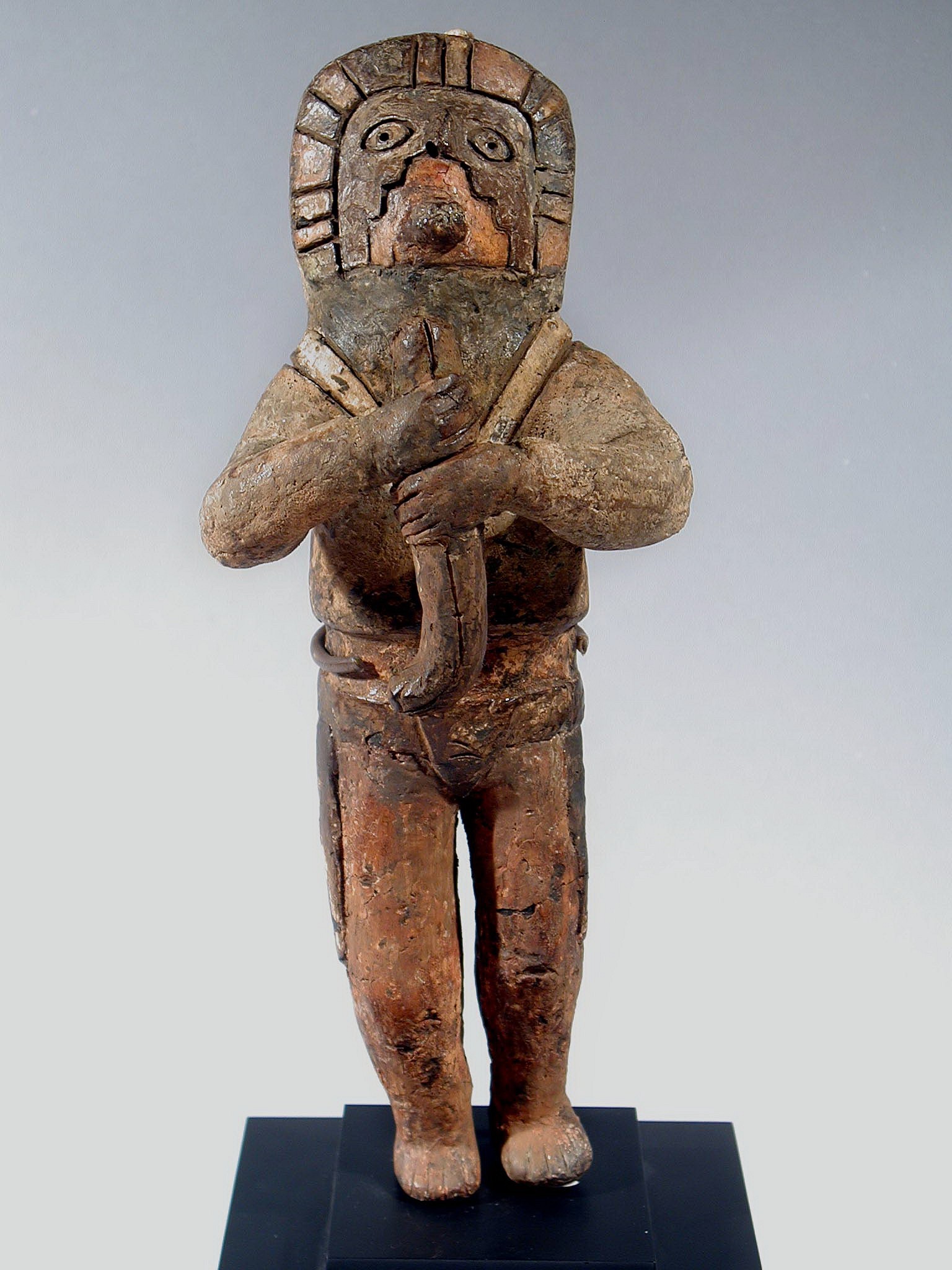 Peru, Chavin carved wood effigy of a shaman
Carved wooden effigy of a standing shaman holding a flute or serpent in front.  The shaman has puckered lips as if he is whistling and appears in a trance like state.  He is wearing a headdress, v neck tunic and belt with two long devices hanging down along the outside of each leg.  On the back of the belt is a "U" shaped device of unknown use.  From the top of the head emeniates a bone tube which has been broken.   A similar shaman's face is illustrated in PRECOLUMBIAN ART OF SOUTH AMERICA by Alan Lapiner fig. 13.    Wooden effigy figures are extremely rare and do not survive well.   The left leg was broken off and re-attached and the evidence of age was apparent.
Media: Wood
Dimensions: Height 9.1/2"
Price Upon Request
95057