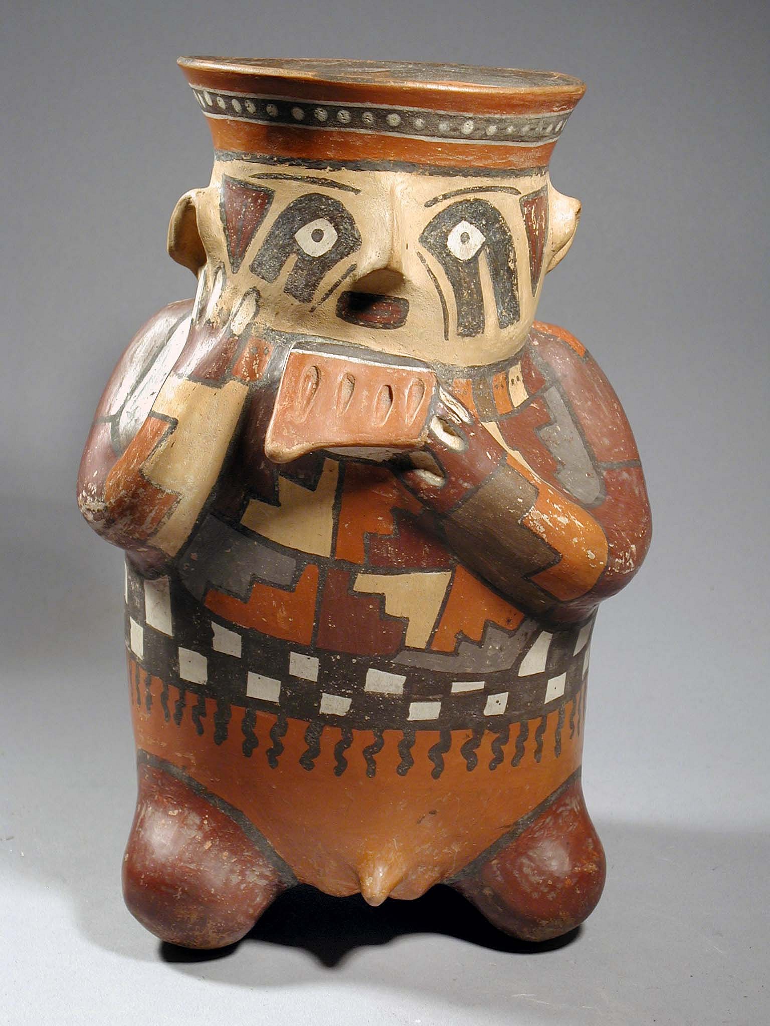 Peru, Nazca Polychrome Effigy Jar with Flute Player
This is one of the few effigy figures in the Nazca ceramic sequence that portrays a musician. The figure is holding a five chambered panpipe in his right hand and has his left hand to his cheek. He is elaborately dressed in patchwork tunic, with a black and white checkered undergarment. Around his neck is a series of plaques in alternating colors of beige, brown and gray. On top of his head is a polka dot band in grey. Below he is wearing a red/brown loin cloth covering prominent genitals. The musician has facial decoration, including black condor profile heads around the eyes and red triangles in front of his ears. This figure is illustrated by Lavalle "Nazca"  (1986: 132).
Media: Ceramic
Dimensions: Height 9 1/2"
$14,000
M3015