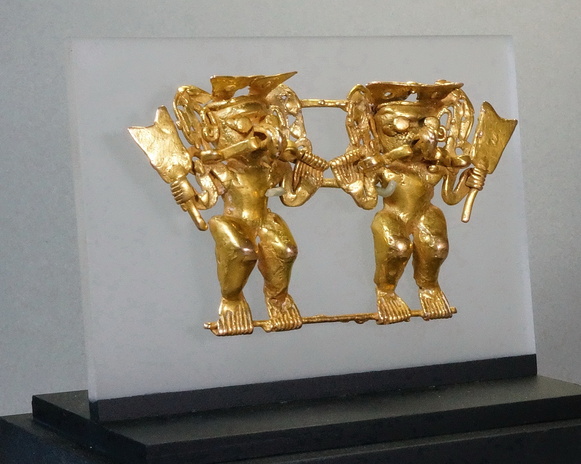 Panama, Cocle Cast Gold Anthropmorphized Twin Warriors
Each warrior has human bodies with bird-like facial features.  They are wearing headdresses with undulating serpents and holding a typical paddle-like standard.  There are curved bands emanating from each of the warrior's mouths.  The warriors have beaked noses, representing transformation into condors.  Ex. New York collector, prior to 1970. Two examples of attached figures are in the Met Museum.  
Period: Panama, Cocle, c. AD 800 - 1200
Media: Metal
Dimensions: Height: 2" x Width: 4"  Weight: 62.5 grams.
Price Upon Request
n7033