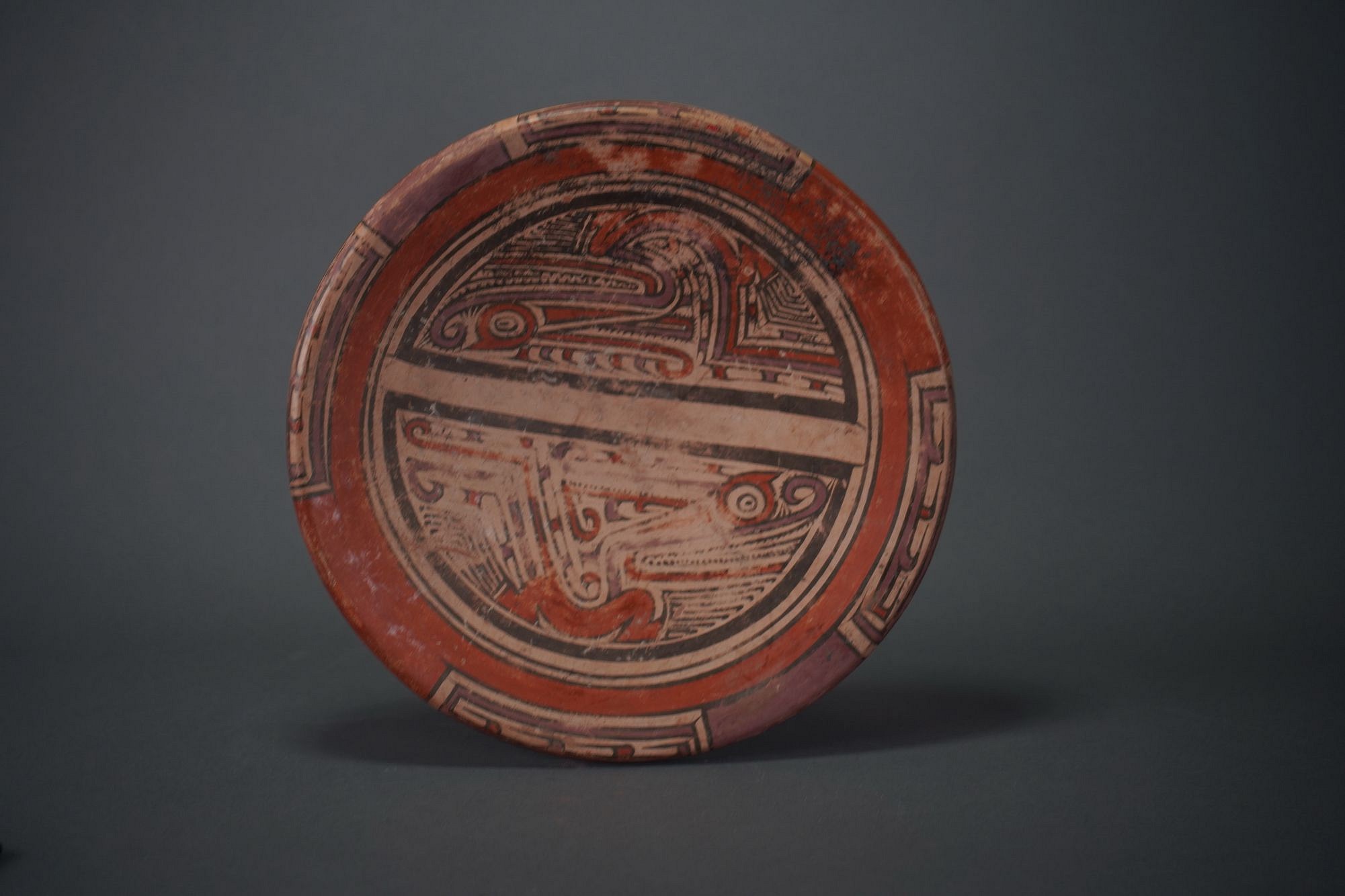 Panama, Macaracas Stye Ceramic Dish Decorated with Stylized Pair of Saurians
The Saurian figures appear in profile in opposite directions and are separated by a narrow band.  Violet and red pigments are used to skillfully define the shapes of the creatures.  The Saurian figures appear on the front, back, and sides of the dish.  Similar saurian designs are illustrated in GUARDIANS OF THE LIFE STREAM by Armand Labbe, fig. 41.  Ex- Los Angles collection.
Media: Ceramic
Dimensions: Diameter: 7 1/2"
$1,650
P1056