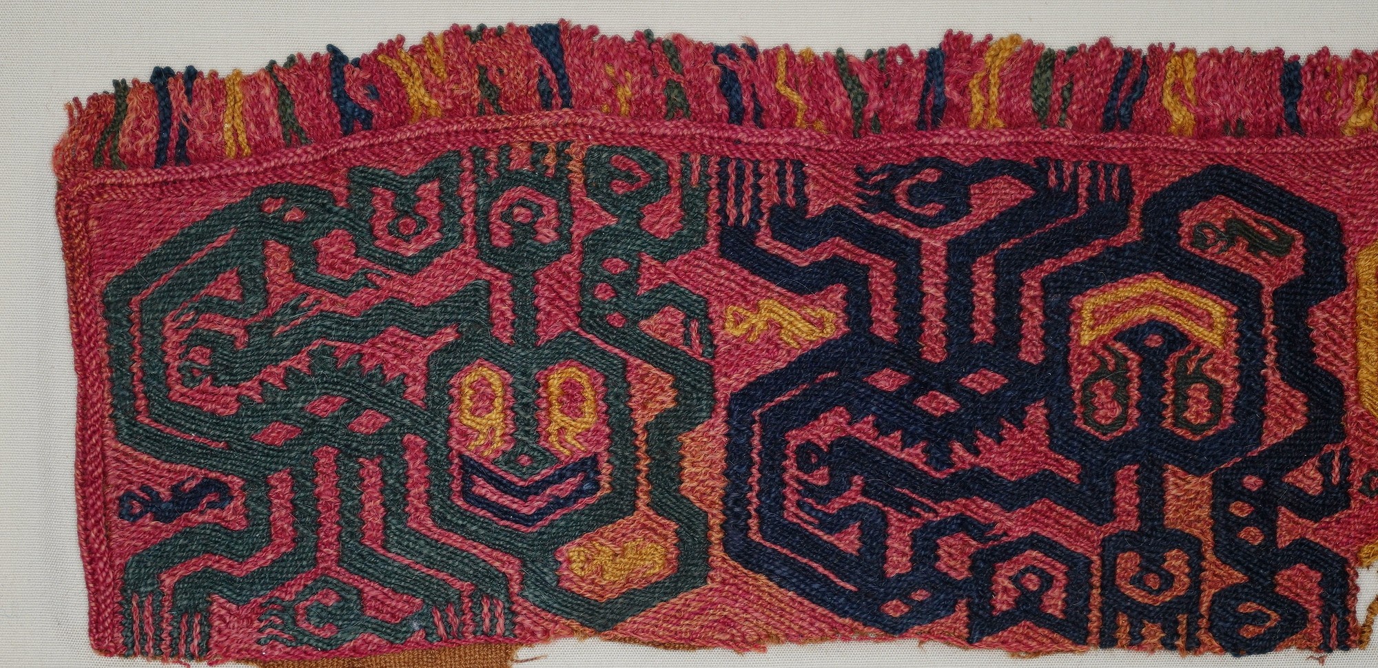 Peru, Paracas  Border Section with Three Colorful Felines on Red Gound
Paracas textiles served as a medium of communication between the realms of the living and the dead.  This Linear style border section features three embroidered feline figures in alternating colors and positions.  One edge has its original fringe intact.  The feline figures represent the "Oculate Being," a prevalent theme occurring throughout the Paracas period.  Here the feline motif is presented with an oversized, characteristically heart-shaped head with a wide smiling mouth and hexagonal eyes.  Another geometricized form springs from the center of each of the feline heads.  Long slender appendages forming the legs of the creatures end in forked claws or transform into smaller feline creatures.  The plain weave red background and embroidered Oculate Being motifs are woven in green, blue, and yellow, creating a beautifully vivid contrast.  This style is characteristic of the textiles that were found at the Necropolis at Wari Kayan.  This textile is from the Early Horizon, Epoch 10.  It is also illustrated in ANCIENT PERUVIAN TEXTILES by Ferdinand Anton, London, 1984, fig. 47.  Ferdinand Anton collection prior to 1980. Good color and pressure mounted in a frame. Period: Peru, Late Paracas, South Coast, c. 300 - 200 BC

Media: Textile
Dimensions: Height: 3" x Length: 12"
$3,250
92016