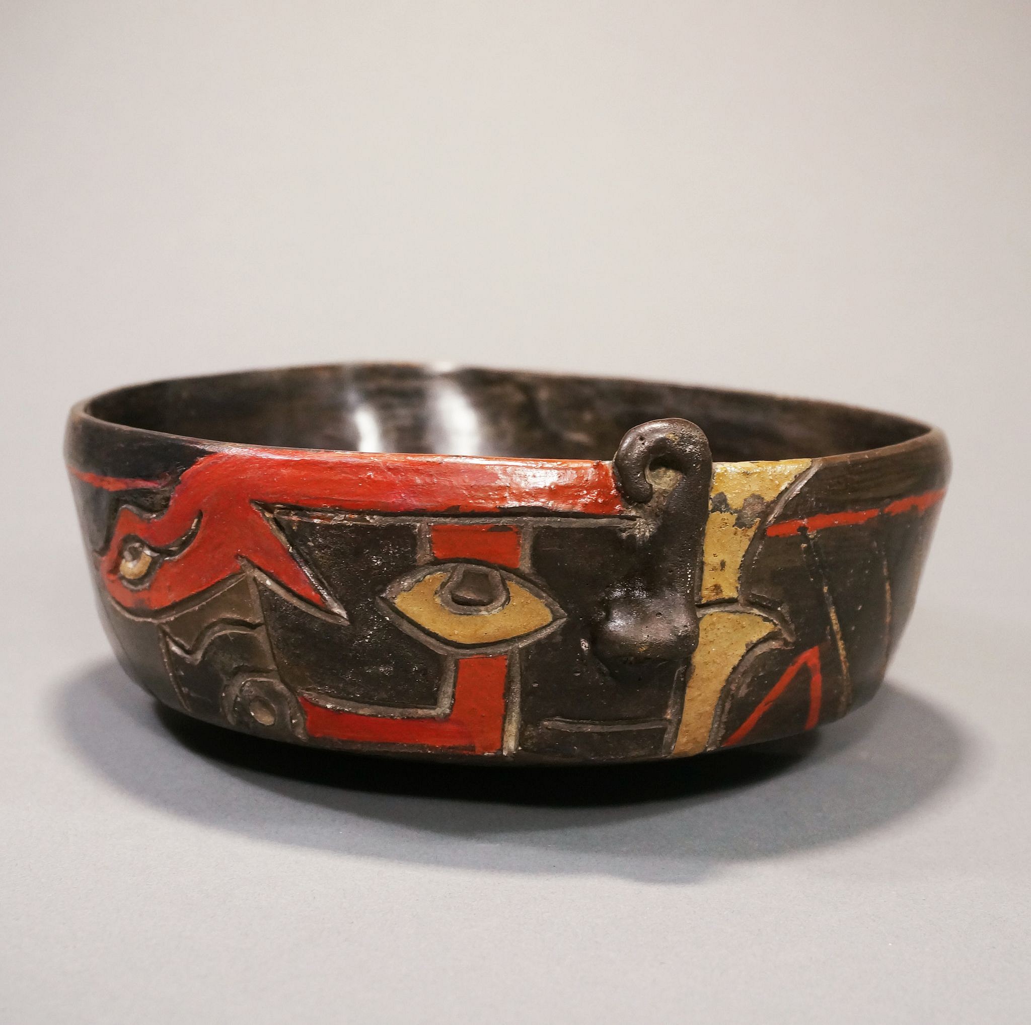 Peru, Early Chavin/Paracas Bowl with Transforming Cubist Face
This bowl demonstrates a human face with a distinct eye looking outward, transforming into the face of a feline entity.  The red serpent above the eye suggests the presence of a supernatural demon or perhaps a knowledgeable serpent spirit guide offering wisdom.  The incised designs are painted with polychrome resin pigments and has an extended lip on the rear upper edge, which was used to pour ritual libations - perhaps Ayahuasca or a similar psychedelic brew containing DMT from entheogenic plants found in the region.  This bowl is also an excellent example of the geometric abstract style with bold blocks of color favored by the Paracas.  It shares stylistic traits with the modern Surrealist and Cubist movements, featuring a morphing of narrative portraiture and purely abstract form.  Ancient art objects with abstract and surrealist qualities were highly sought after by sophisticated collectors with excellent taste during the mid-20th Century.  These collectors would combine ancient and modern artworks together, forming a unified gestalt aesthetic.  Abstraction is quite rare among pre-modern societies, and one hypothesis as to why the Andeans had such a sophisticated understanding of abstract form and color is the entheogen theory.  In his 2005 paper Psychoactive botanicals in ritual, religion and shamanism, Glenn H. Shepard discusses how Chavin de Huantar, the main Chavin temple, was located near a geologic unstable valley region in the Andes with a wealth of natural plant entheogens where two rivers merge.  The Chavin people believed that the spirit could transcend the body and fuse with the spirit of the jaguar, a belief that was likely facilitated by entheogen use.  This animistic belief system affected all subsequent Andean cultures, including the Paracas, whose would continue this belief.  This bowl depicts a human face with a distinct eye, transforming into a jaguar spirit with a bright red serpent framing the eye.  The red serpent suggests the presence of a sentient serpent demon or perhaps a knowledgeable spirit guide offering wisdom.  
A very similar vessel is in the Oscar Landmann collection #119, Sao Paulo, Brazil. Ex-Collection Anton Roeckl, Germany.
Note: The bowl was painted within the incised designs with post-fired polychrome resin pigments and finished after firing with a second firing to melt the resin creating a glossy finish.  This tradition began with the Chavin cult, a psychedelic cult that engaged in ritualistic jaguar worship. Using psychedelics, one could transcend the body and become the spirit of the feline.  The Chavin influenced all subsequent Pre-Columbian cultures, including the Paracas, who would continue this belief.  This bowl demonstrates a human face with a distinct eye looking outward, transforming into the face of a feline entity.  The red serpent above the eye suggests the presents of a supernatural demon or perhaps a knowledgeable serpent spirit guide offering wisdom to the transforming shaman.  This design demonstrates an animist belief in an interconnected network of souls and spirits. Period: Peru, Paracas, Ocucaje, c. 500 BC -  AD 100 
Period: Peru, Paracas, Ocucaje, c. 500BC - 100AD BC
Media: Ceramic
Dimensions: Height: 2 1/2" x Diameter: 7"
$22,500
M7134