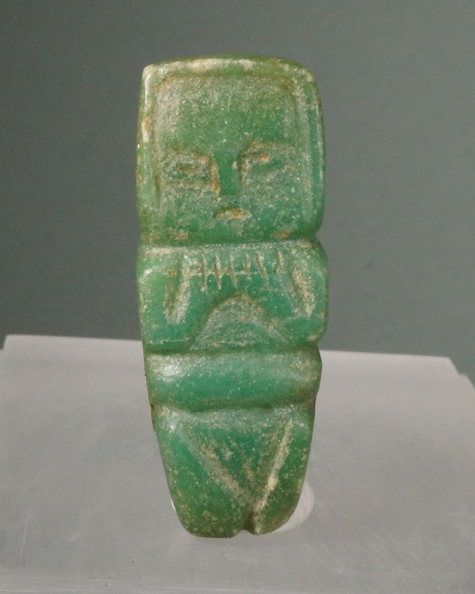 Dominican Republic, Taíno  Carved Greenstone Venus Amulet
This greenstone female figure is carved in low relief with arms crossed over her chest and a baby strapped in a bundle on her back.  This amulet is decidedly rare for its maternal aspect and its naturally symbolic association to fertility.  The stone is a rare form of green quartz.
Period: Dominican Republic, Ostionoid, c. AD 200 - 900
Media: Stone
Dimensions: Height: 2 1/4"
98140