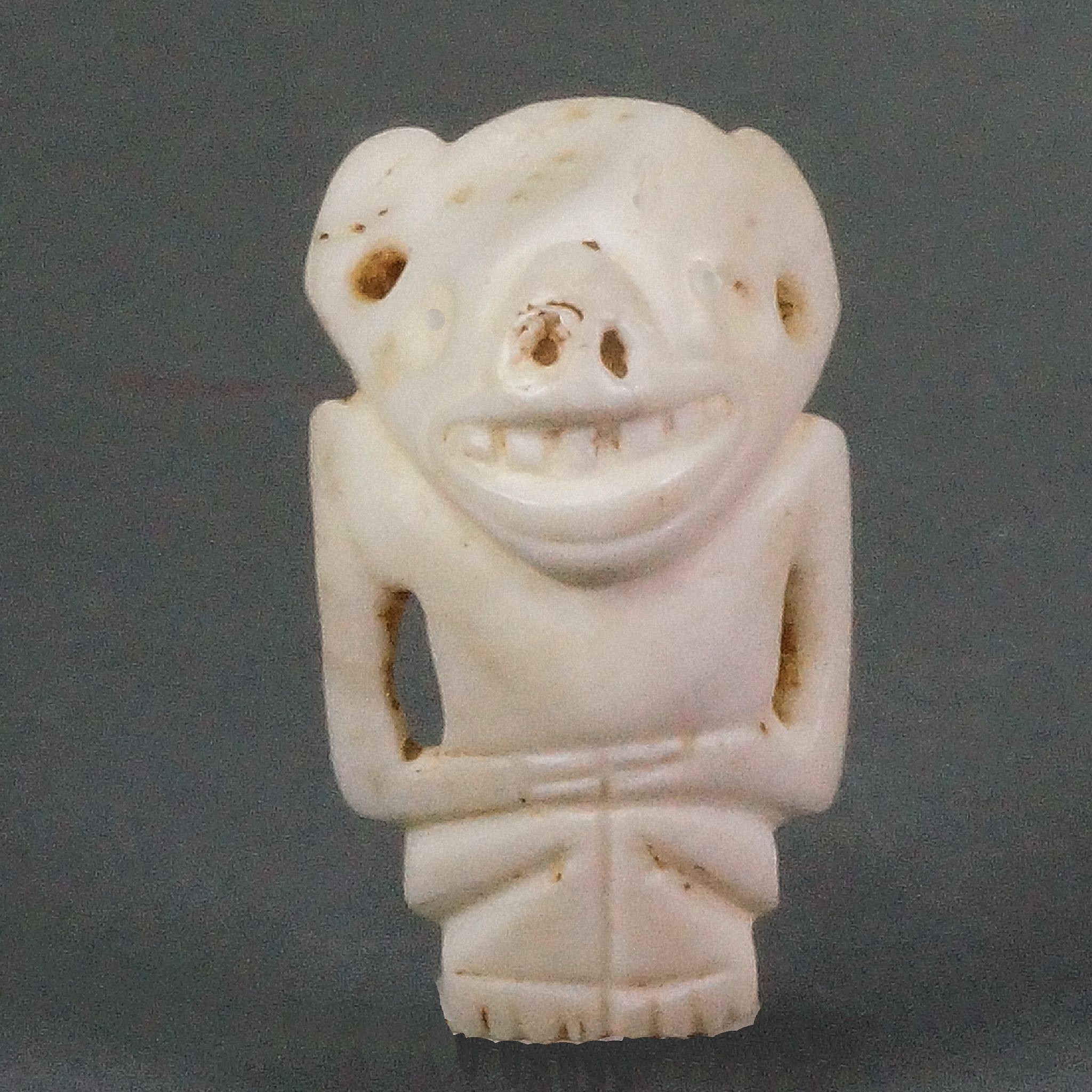 Dominican Republic, Taíno Carved Shell Amulet of a Figure with a Bat Face
This bat deity amulet features a stylized human figure with bat-like features, such as large ears and a pug nose.  There are two suspension holes below each ear.  This amulet was likely originally the central bead on a larger beaded necklace.
Period: Dominican Republic, Taíno , c. AD 1000 - 1500
Media: Shell
Dimensions: Height: 1 1/2"
98149