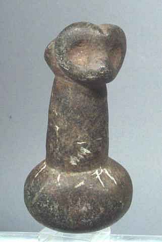 Dominican Republic, Taíno Carved Dark Stone Pestle with Owl Deity
Seen straight on is the face of an owl with large eyes and heart-shaped face.  Seen from above is an abstract face that represents an animal with large eyes and a pudgy nose, possibly a dog.  The round lens lends itself to crushing seeds.
Period: Dominican Republic, Taíno , c. AD 1000 - 1500
Media: Stone
Dimensions: Height: 6"
98429A