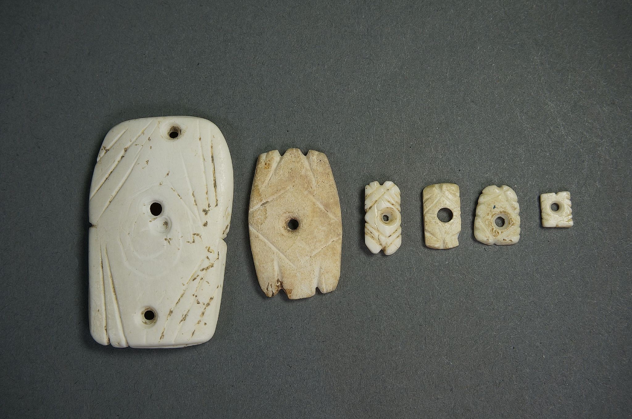 Dominican Republic, Six Taíno  Miniature Shell Highly Abstract Frog Ornaments
Frog-shaped amulets were often worn as protective charms in memory of important ancestors. These examples have amulet suspension holes as well as vertical drill holes, suggesting that each frog was made in the same abstract linear format in descending size.  The smallest frog in this group is one of the smallest known pieces of its kind.
Period: Dominican Republic, Taíno , c. AD 1000 - 1500
Media: Stone
Dimensions: Height: 1/4" to 1 1/4"
99359