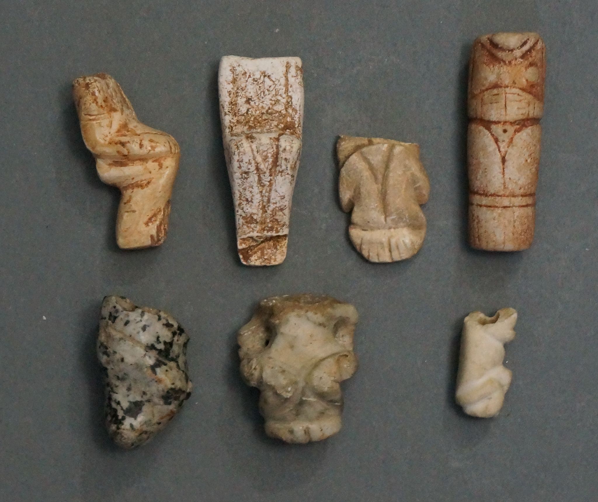 Dominican Republic, Seven Broken Figurative Amulets of Different Materials
These broken amulets are historically significant because the broken points reveal the method of carving and drilling. They all seem to have been broken at the horizontal suspension hole.  The amulets were not discarded; they were found in tombs and were valued even as fragments.  Several of the pieces still have traces of red pigment.
Period: Dominican Republic, Taíno , c. AD 1000 - 1500
Media: Stone
Dimensions: Lengths  vary from 1/2" to 1"
99390