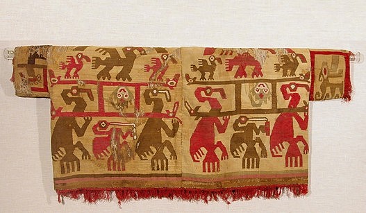 Peru, Tapestry Shirt with Anthropomorphized Pelicans Carrying Manta-Ray Deity
This tapestry woven shirt with short sleeves was crafted with cotton warps and camelid wefts in red, brown, olive green and white on a yellow-ochre ground. The backs of the panels display the same scene in reverse colors.  The elaborate ritual procession portrayed by this textile was likely the result of an entheogen-induced vision seen by a highly skilled shaman or artisan. A manta ray deity, identifiable by his tail and large, flat eyes, is elevated on a litter carried in exaltation by anthropomorphized cormorants. Litters were a prestigious mode of transportation along the North coast of Peru, indicating the
importance of the manta deity. Large manta rays live in the waters off the Pacific coast of South America, and these marine animals are extremely beautiful and majestic. A small brown pelican appears to imbibe a psychedelic brew, while the poles that make up the litter transform into eels &ndash; revered in Andean mythology for their ability to transition between land and sea. This imagery would have been extremely important to the Pre-Columbian psyche as their survival was contingent upon the appearance of healthy manta rays and pelicans. Rays feed upon plankton and other small marine life. These smaller life forms carried by the ocean currents would die off during disastrous climatic events such as El Ni&ntilde;o. The sight of a healthy manta ray along the coast would be a cause for celebration as mantas were an indicator of the return of a prosperous fishing season. Pelicans are equally crucial to the Peruvian ecosystem. They are excellent fishers and produce valuable guano (fertilizer; in the Chimu&rsquo;s animistic worldview, the appearance of pelicans would have been a harbinger of prosperity. The return of the manta-ray together with the pelicans signals the health of the biosphere, and an abundance of fish for both the pelicans and the human population. A healthy ocean was a cause for festivities. This tunic was formerly in the collection of the Southwest Museum outside of Los Angeles. It is illustrated in Ann Rowe&rsquo;s Costumes and Featherwork of the Lords of Chimor. Acquired in 1995 from a New York gallery. 

Period: Peru, Chimu, North Coast, c. AD 900 - 1350
Media: Textile
Dimensions: Width 47-1/2" x Length 19-1/2"
Price Upon Request
96127